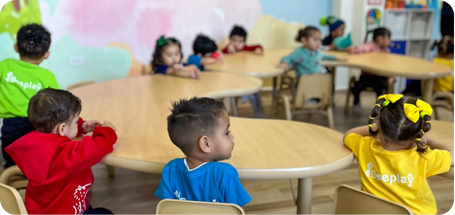 Niños sentados en mesas redondas en el aula.